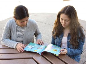 PUBLISHED JUNIOR DUO survey their book, while seated in the quad. After years of hard work their children's picture book, 