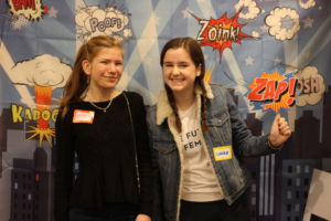 Sophomores Olivia Raskin and Claire Fogarty stand in front of a superhero backdrop before keynote speaker Pamela Hamamoto takes the stage