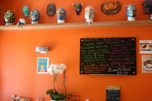 Display of vibrant orange walls where traditional masks from Mexico hang