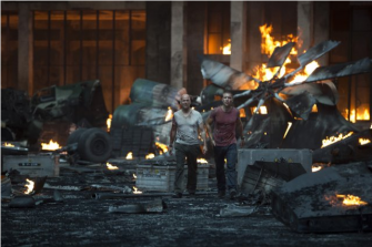 ESCAPING AN EXPLOSION, John (played by Bruce Willis) and his son Jack (played by Jai Courtney) stride away from the flames.