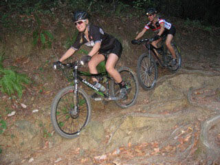 Kelsey (front) and Cameron (back) Urban ride down a trail covered in roots. 
