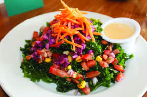 THE ALL-HAIL KALE salad served at Veggie Grill is full of kale, red cabbage, shredded carrots, quinoa,  yellow corn salsa, and almonds with a ginger-papaya vinaigrette.