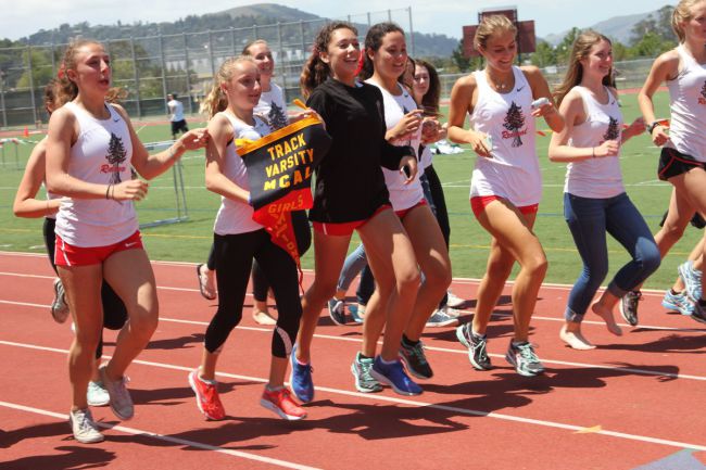 The girl's track team runs around the track with their MCAL pennant. 