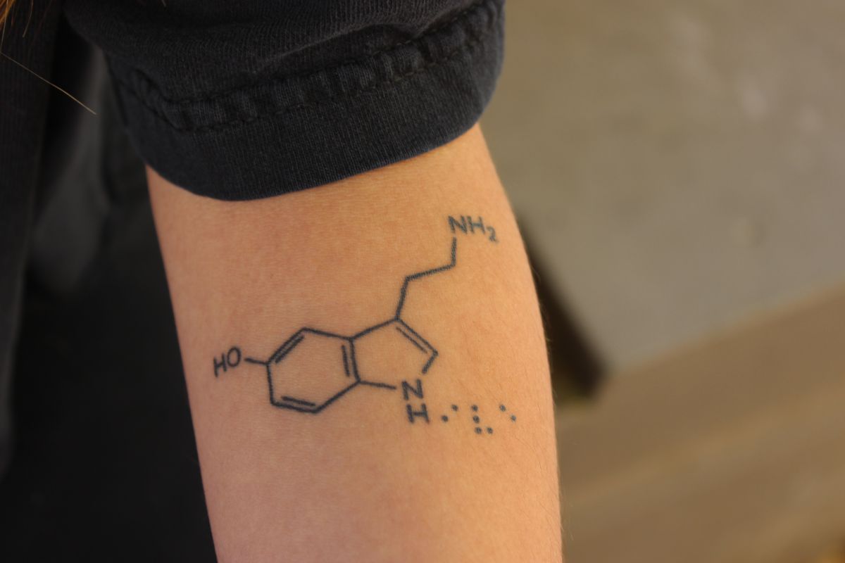 Rodriquez displays a tattoo of a serotonin molecule on her forearm. The dots next to the molecule spell out 