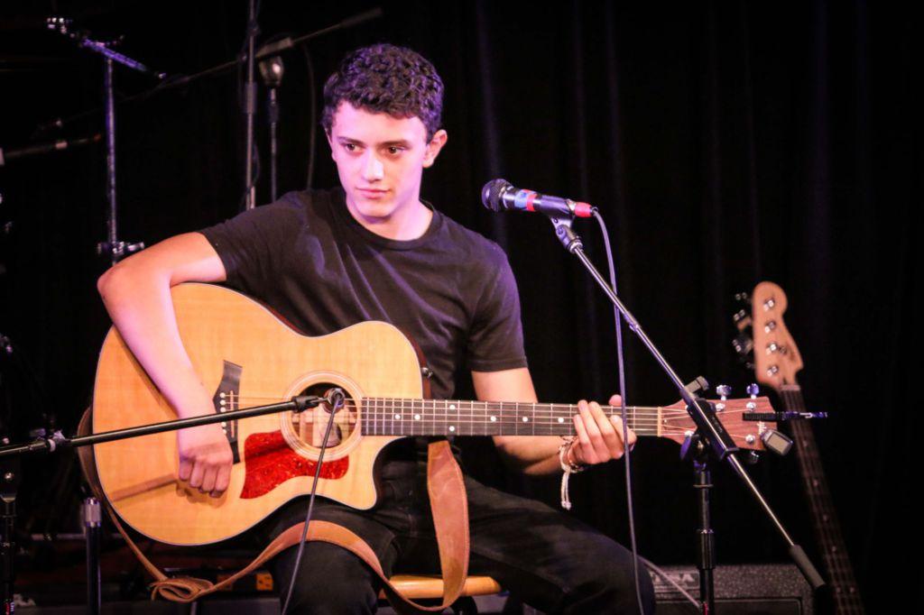 Performing a cover onstage, senior Matty Michna plays his guitar, 