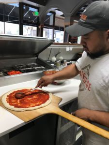 A chef spreads red sauce on dough that has been proofed for 48 hours.