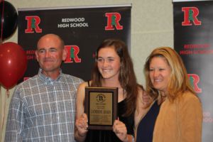Senior Catherine Jensen beams alongside her parents while holding up her coaches award.