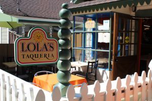 Sidewalk view of Lola's Taqueria includes festive and colorful sign and exterior design 