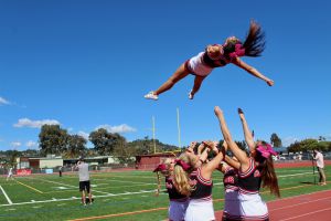 Cheerleaders practice stunts on the sideline.