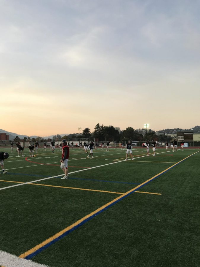 Beginning their warmup, the varsity football team practices under the lights due to soccer tryouts and daylight savings.