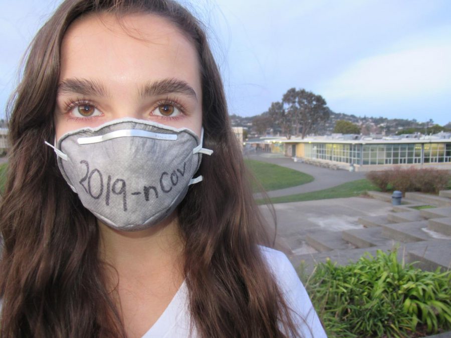 A student stands in front of Redwood’s amphitheater wearing a mask in solidarity with people infected with the novel coronavirus