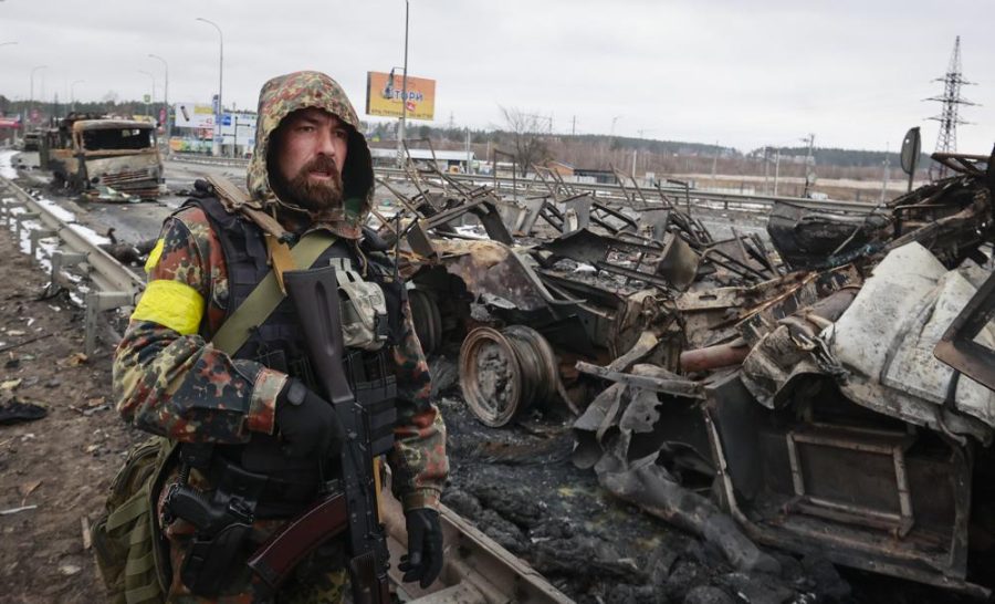 Gripping his rifle, a Ukrainian soldier stands by a destroyed Russian vehicle near Kyiv. (Image courtesy of Serhii Nuzhnenko, AP Photo)