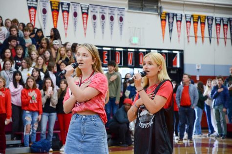 With their hands over their hearts, seniors Julia Ginsburg and Emma Orrick sing the national anthem.
