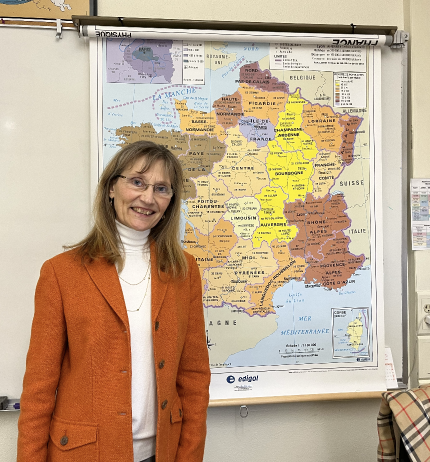Bernadette Rattet smiles in her classroom, standing in front of her map of France.