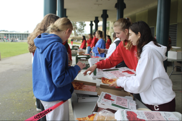 Leadership student Katelyn Van-Dusen hands out pizza to students while wearing her spirited Leadership hoodie, fitting with the red-themed spirit day.