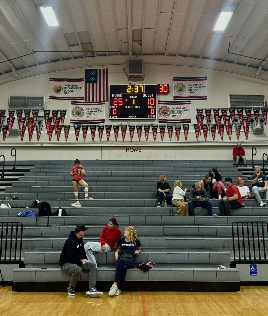 The “home” letters on the back wall of the gym shine brightly, as no student section fills the bleachers at a volleyball game (Photo courtesy of Julia Delsol)