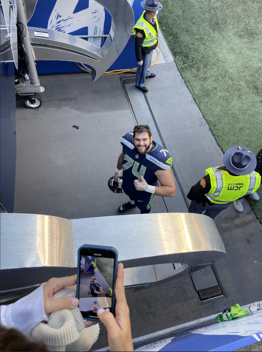 Giving the camera a thumbs-up, Jake Curhan stands beside the field wearing his Seahawks jersey. (Photo Courtesy of Randi Curhan)