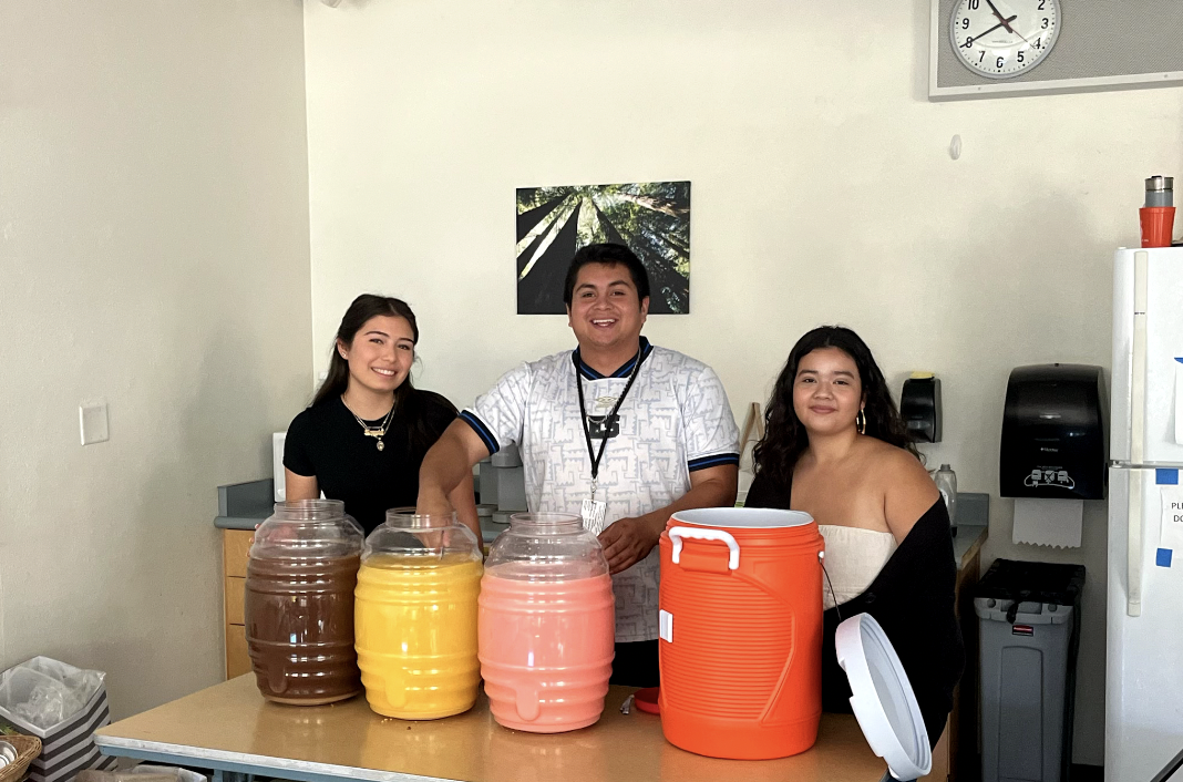 Preparing Agua Fresca for their Hispanic Heritage Month Celebration, Club member and Samuel Chavez (center) and Sara Hernandez (left) stand behind the jugs as they begin to bring them out.