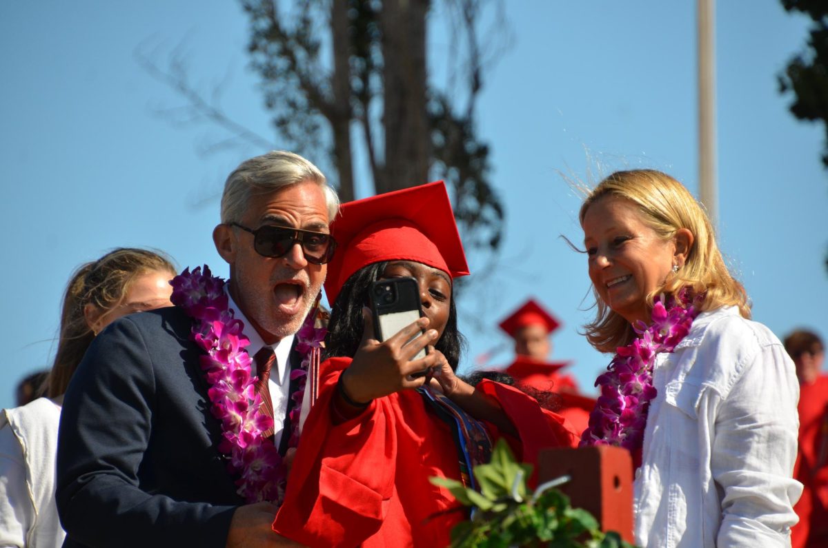 A graduate films as she walks across the stage, taking a selfie with Dr. Payne to help her remember the moment. 