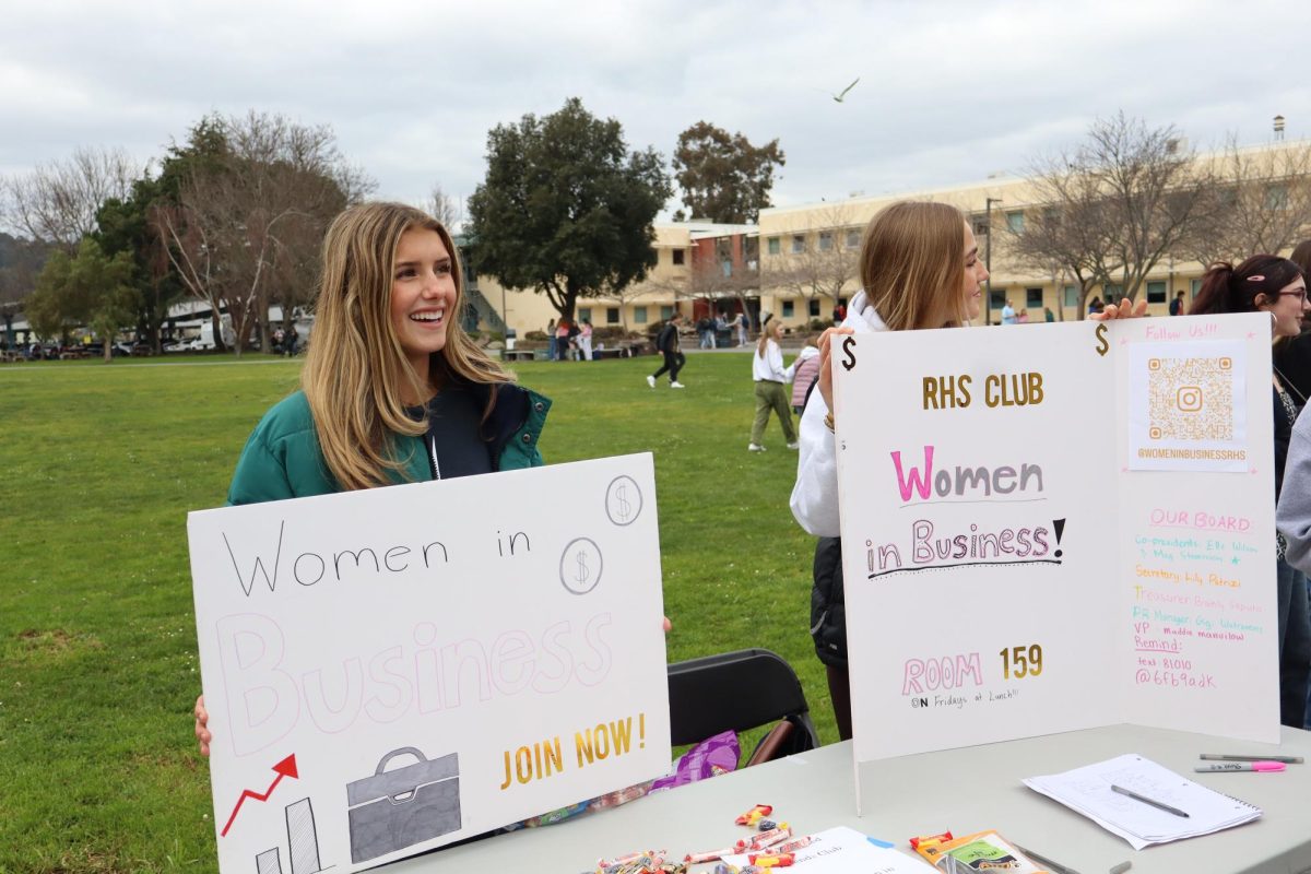 Junior Meg Stevenson holds up a handmade poster to promote her club, Women in Business, and gain attention from the students walking around. 
