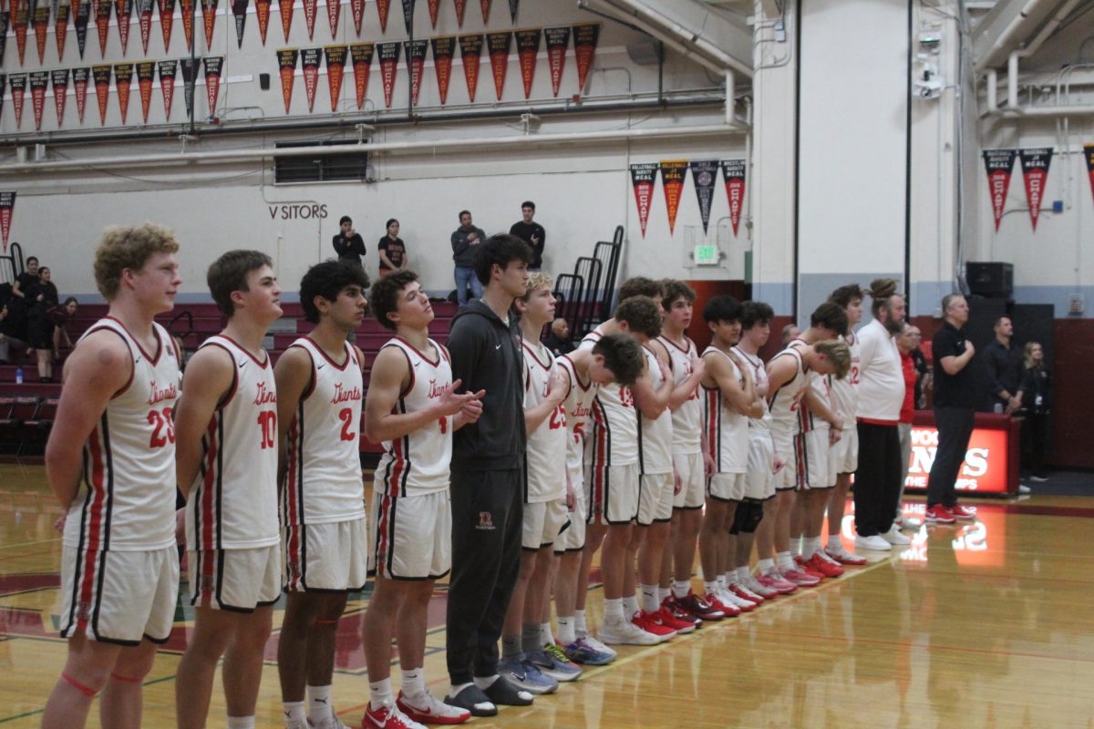 Standing together before the game, the boys’ varsity basketball team lines up during the national anthem.