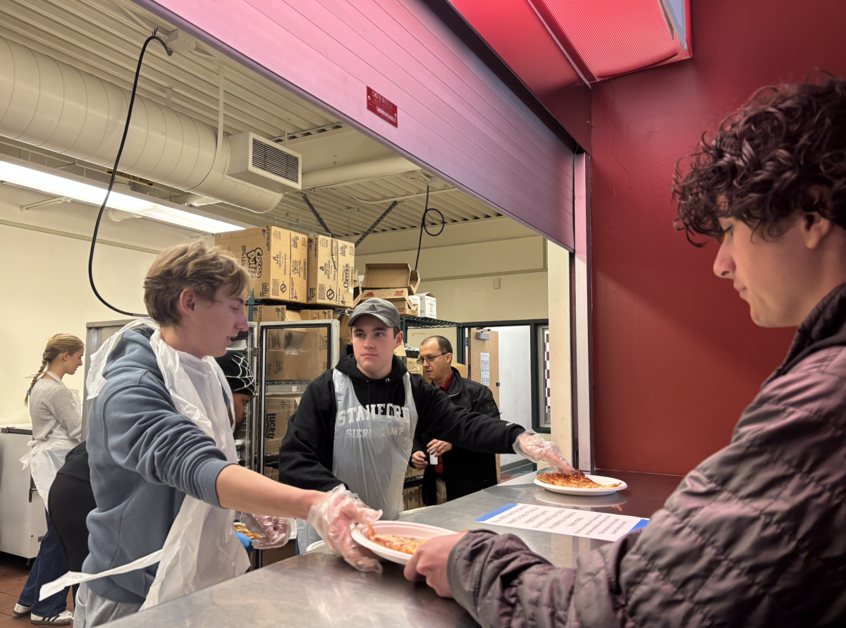 Students pick up fresh pizza inside the cafeteria as freshmen Izzy Glassel and Mason McCabe serve them.
