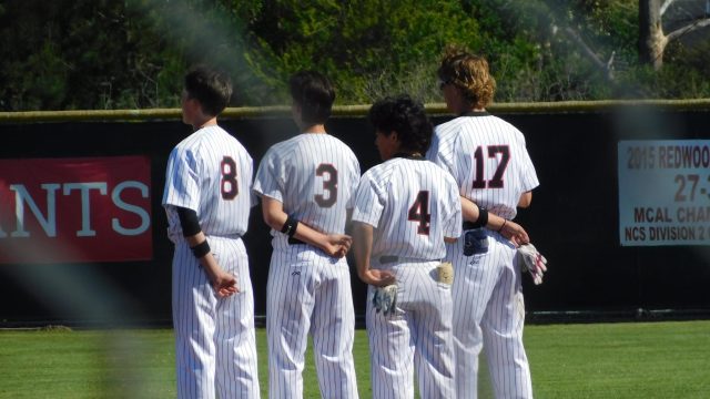 Juniors Kaelin Christman (left), Lucas Ghio (middle left), sophomore Theo Trono (middle right) and freshman Chase Johnson (right) stand over second base during the anthem.